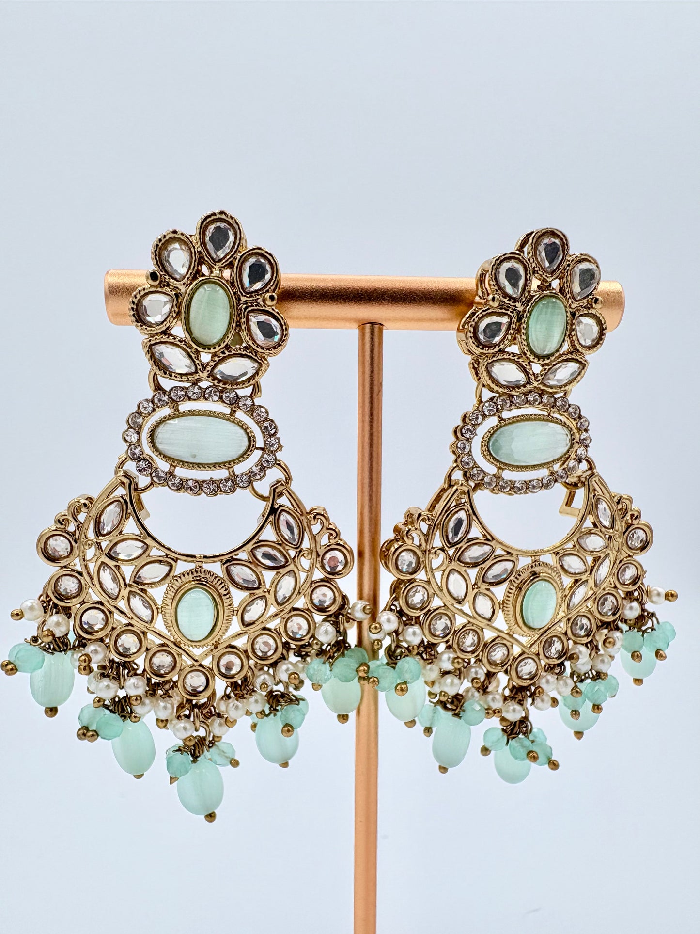 Ornate earrings with gold and green stones on a stand available at Nishaani.ca – Indian jewelry in Canada