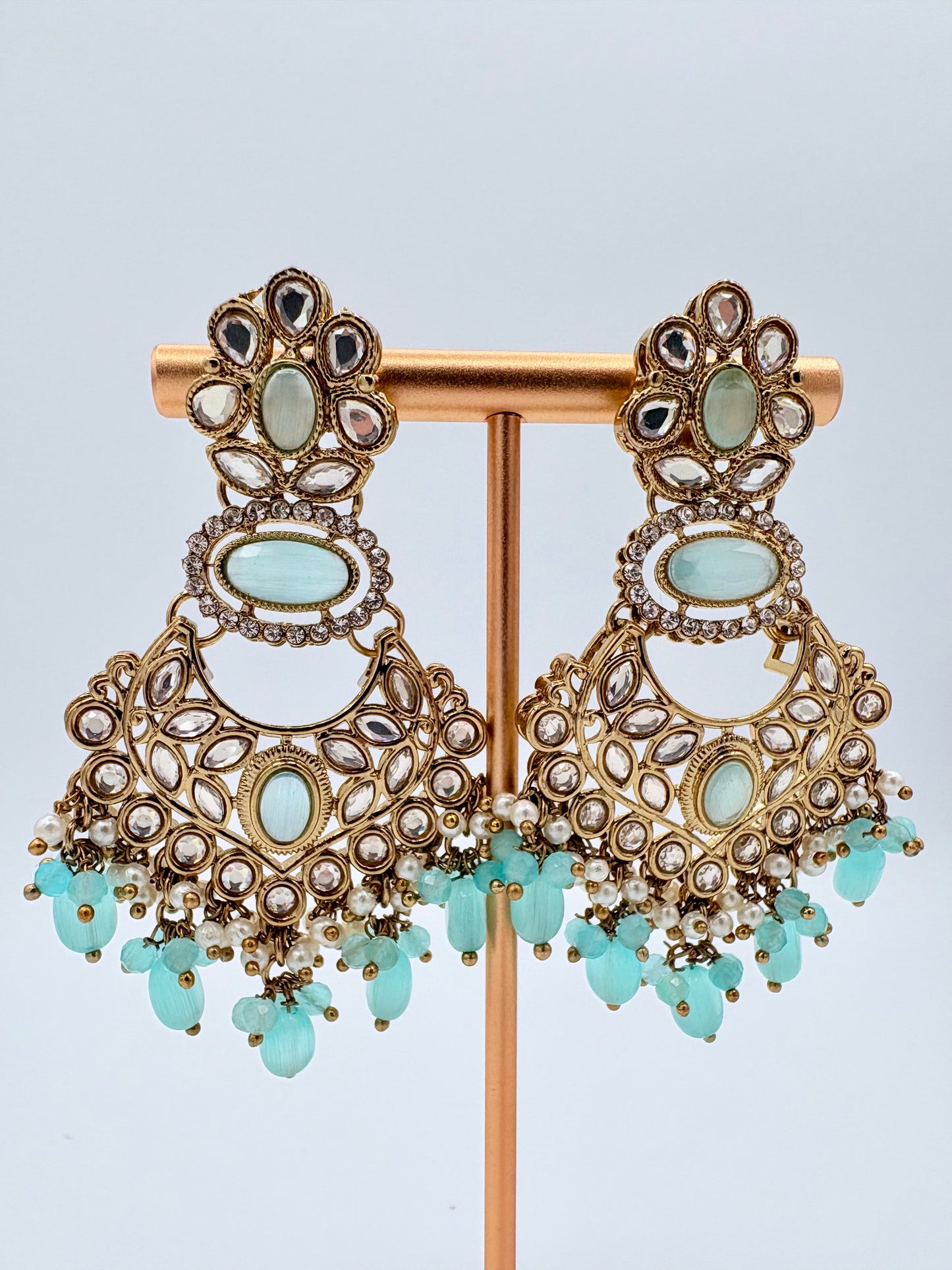 Ornate earrings with gold and turquoise stones on a stand available at Nishaani.ca – Indian jewelry in Canada