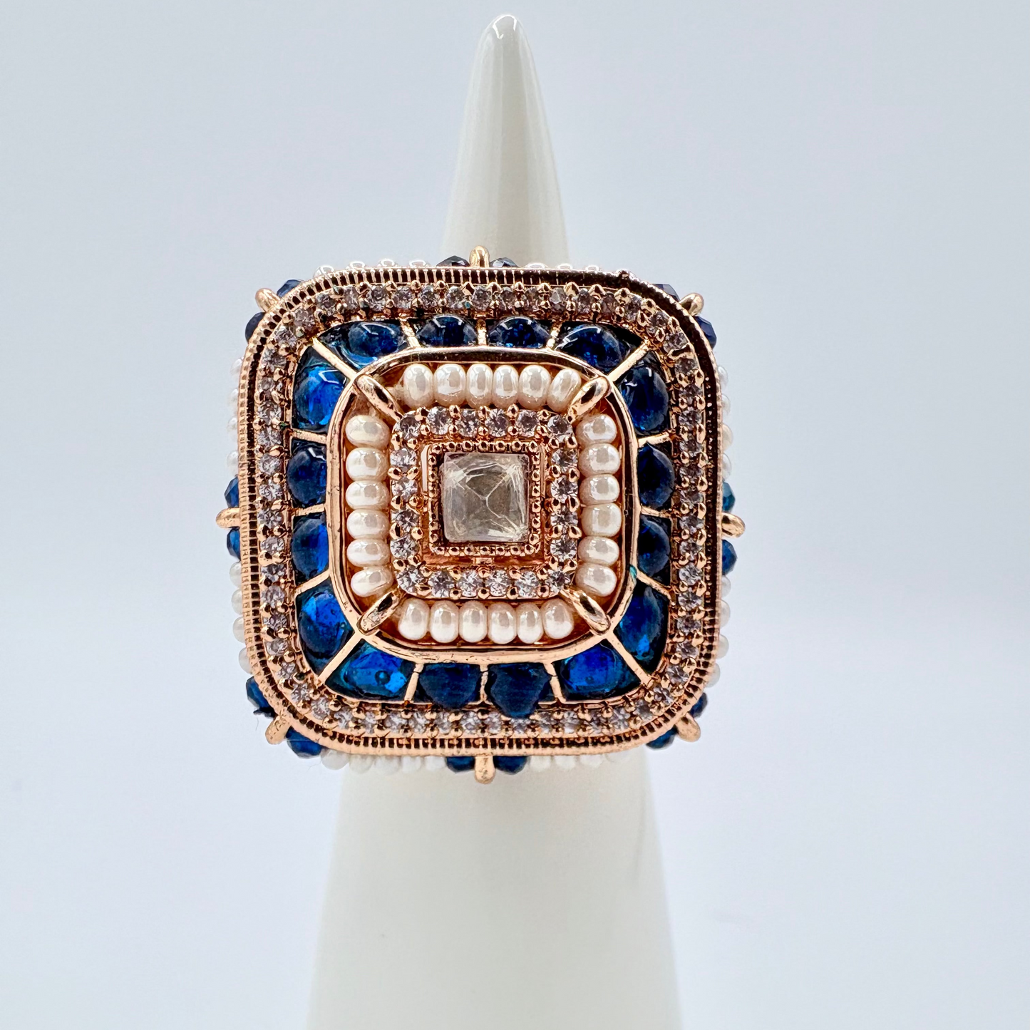 Decorative ring with blue stones and pearl accents on a white stand available at Nishaani.ca – Indian jewelry in Canada