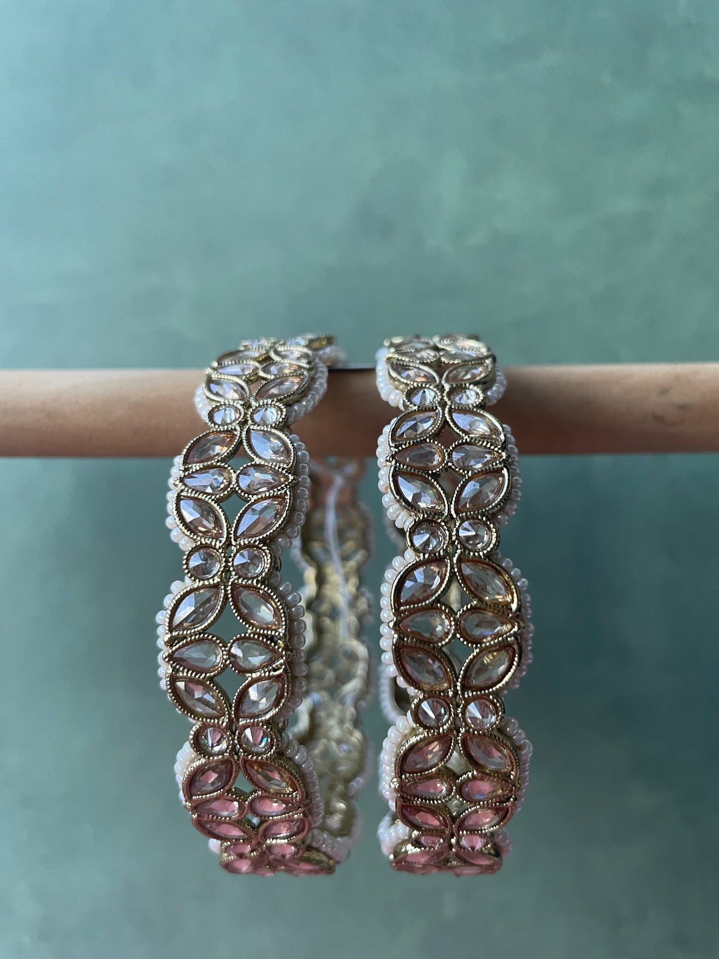 A pair of gold-colored bracelets with floral patterns, featuring pearl-like beads available at Nishaani.ca – Indian jewelry in Canada