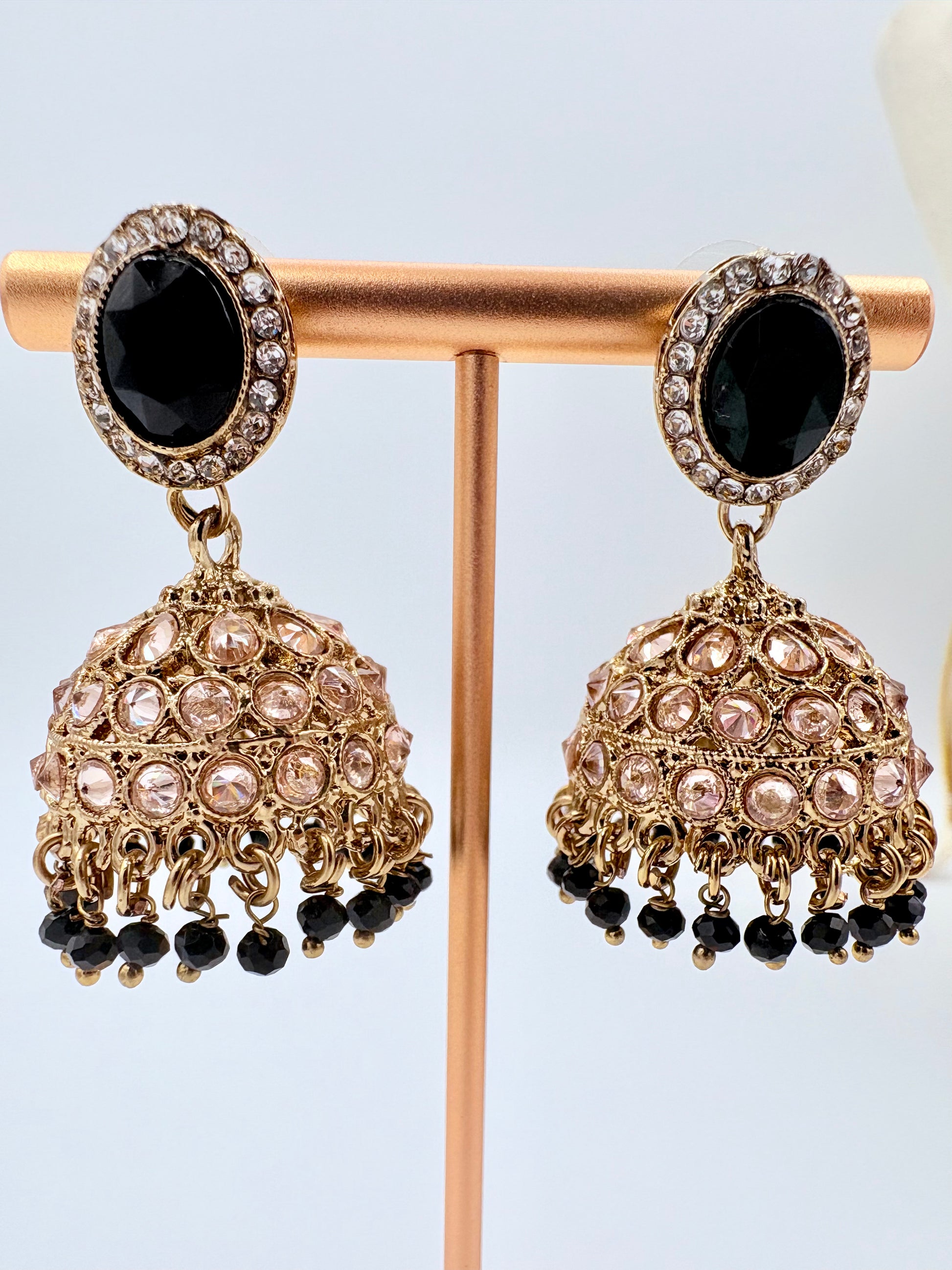 Pair of ornate earrings with black and gold details on a stand against a light blue background available at Nishaani.ca – Indian jewelry in Canada