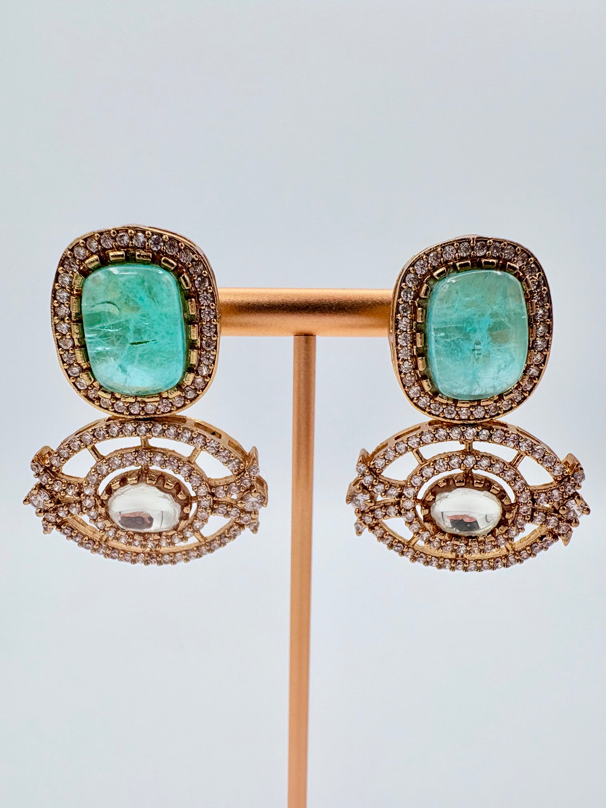 Pair of earrings with turquoise stones and gold accents on a stand against a available at Nishaani.ca – Indian jewelry in Canada