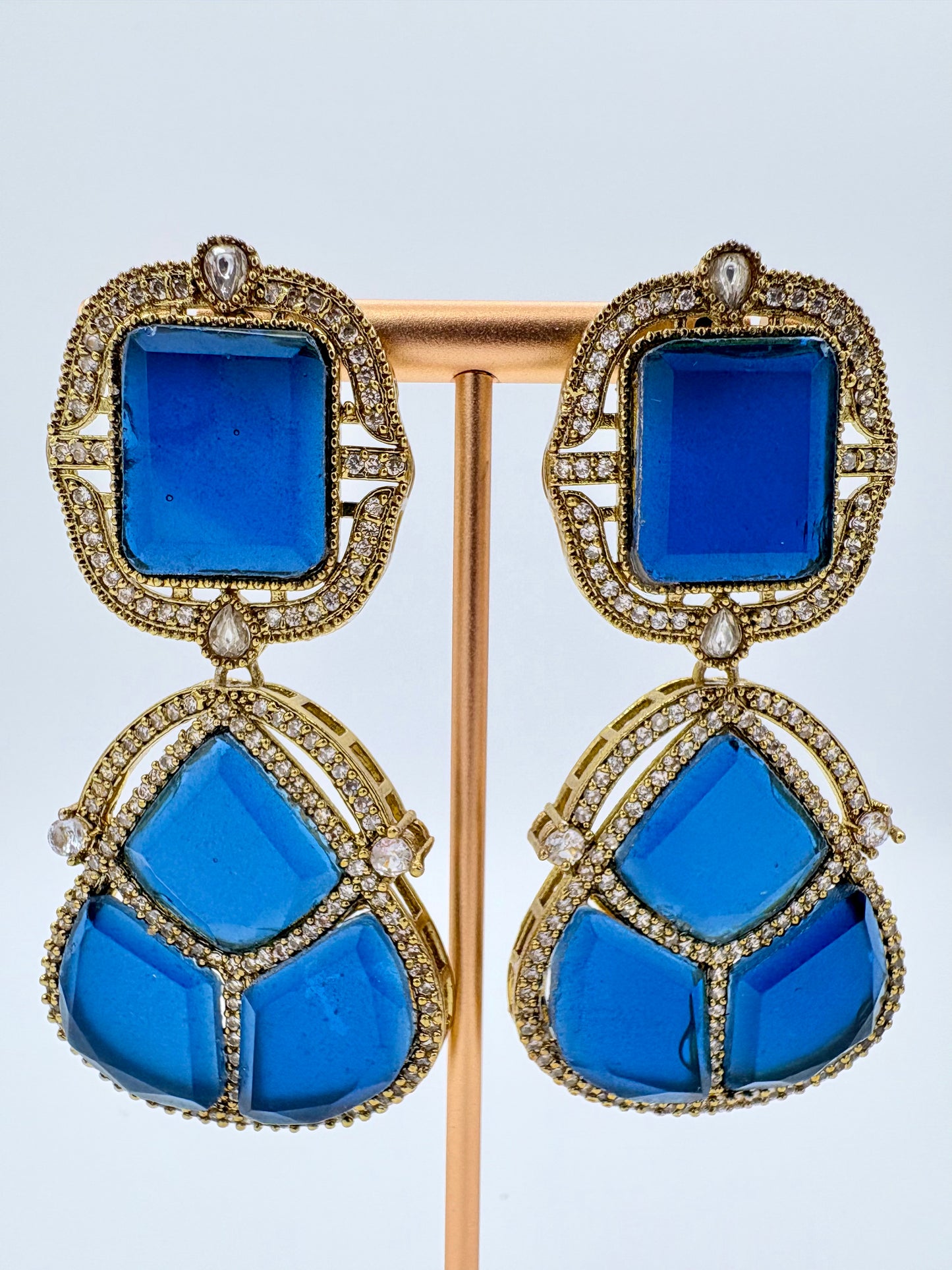 Pair of blue earrings with gold accents on a standavailable at Nishaani.ca – Indian jewelry in Canada