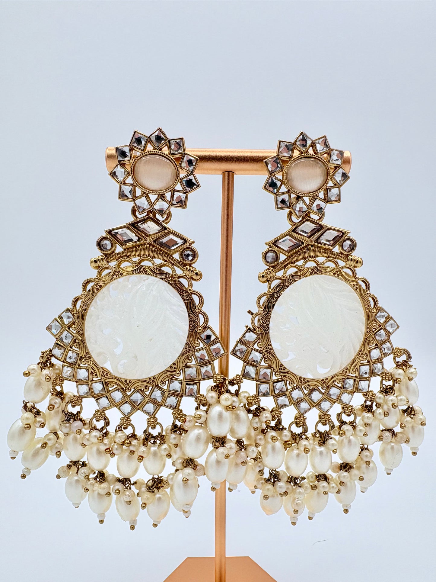 Ornate earrings with gold detailing and white stones on a stand available at Nishaani.ca – Indian jewelry in Canada