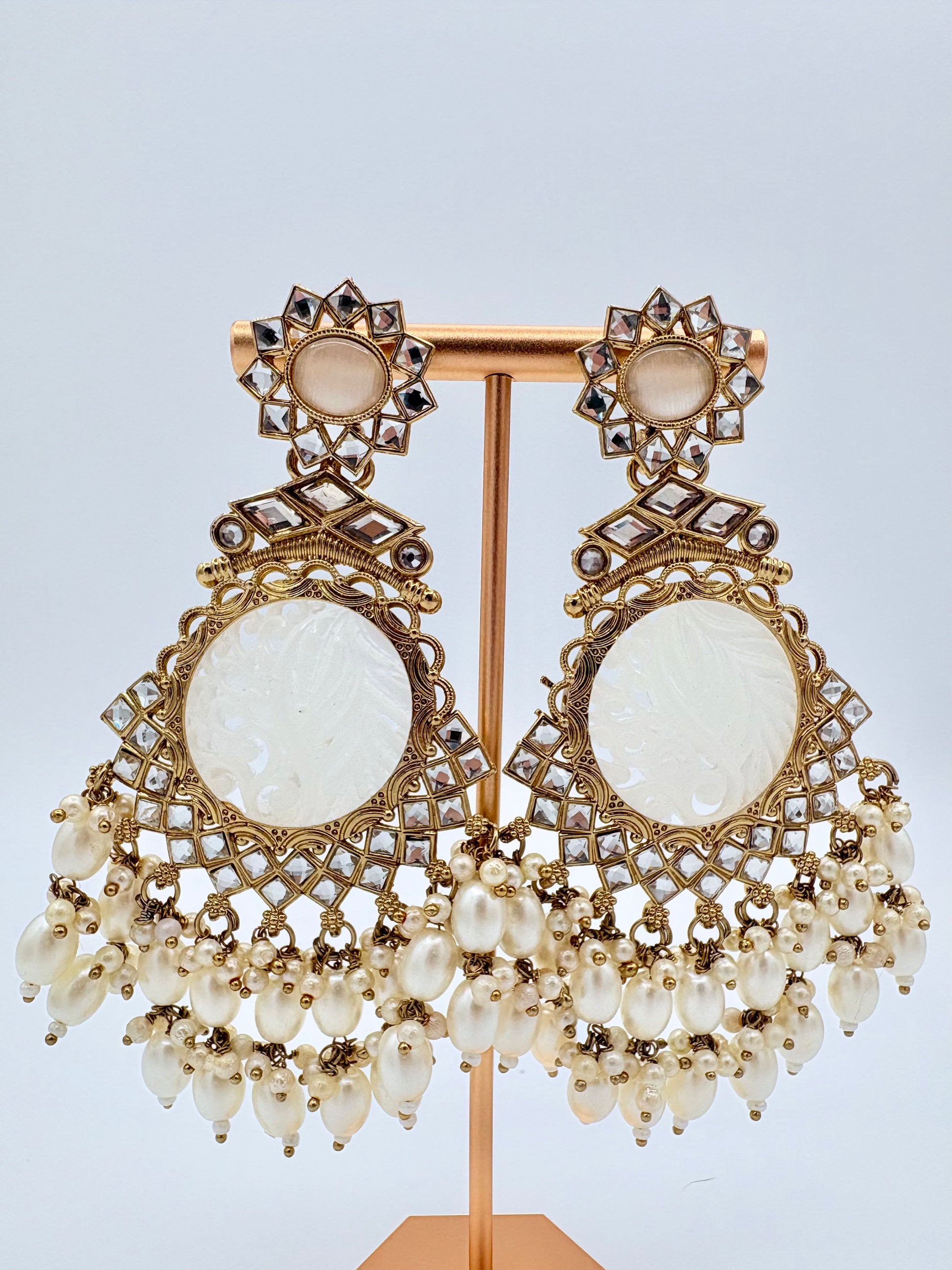 Ornate earrings with gold detailing and white stones on a stand available at Nishaani.ca – Indian jewelry in Canada