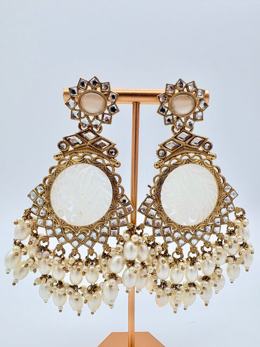 Ornate earrings with gold detailing and white stones on a stand available at Nishaani.ca – Indian jewelry in Canada