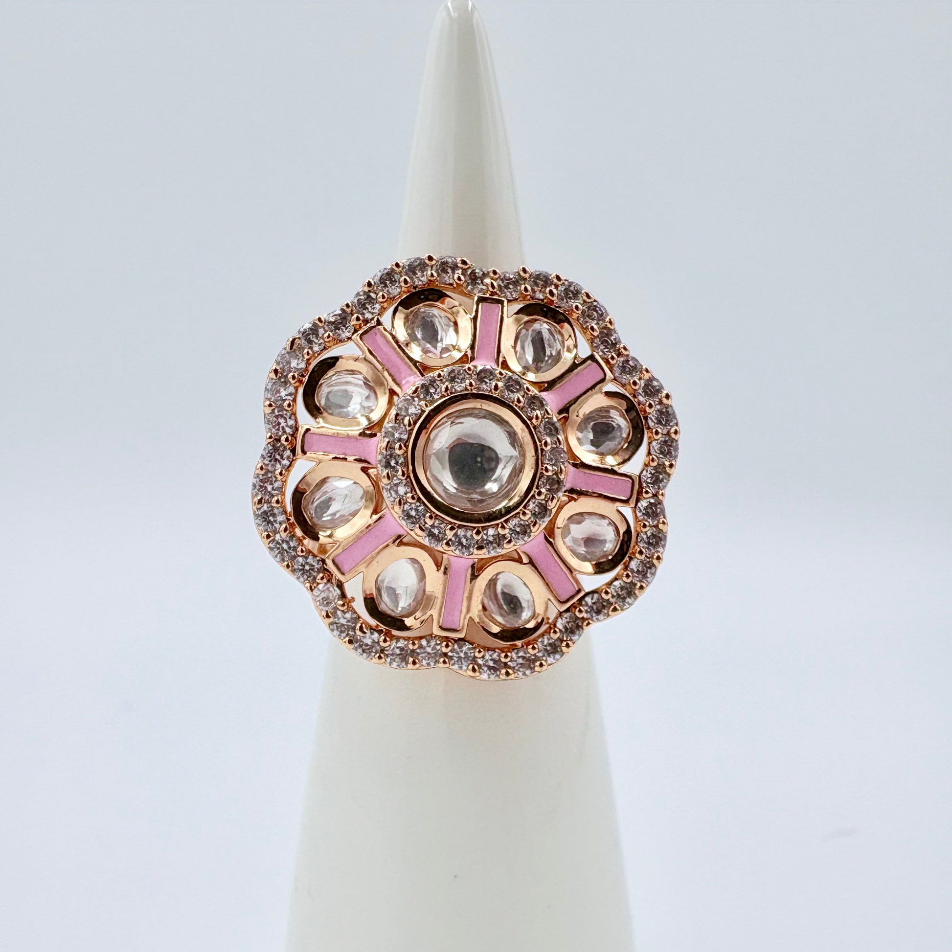 Decorative ring with pink and rose gold accents on a white stand against a light blue background available at Nishaani.ca – Indian jewelry in Canada