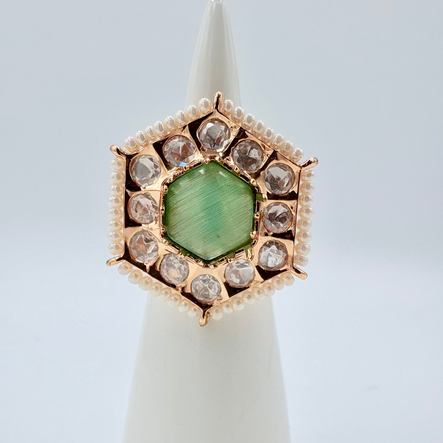 Ring with green gemstone and rose gold accents on a white stand against a light gray background available at Nishaani.ca – Indian jewelry in Canada
