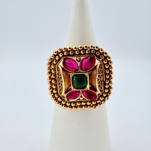Gold ring with red and green gemstones on a white cone available at Nishaani.ca – Indian jewelry in Canada