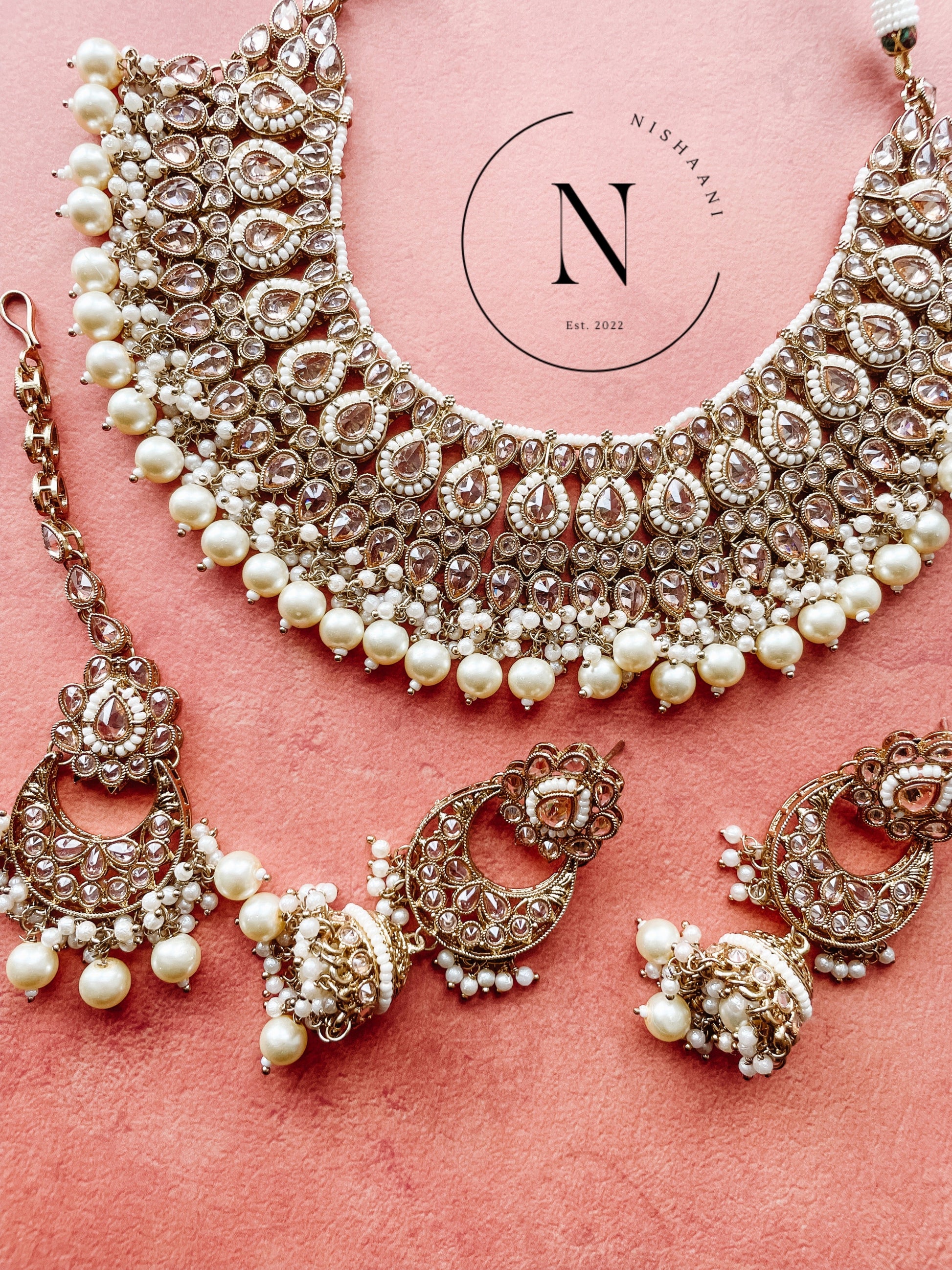 A set of traditional Indian jewelry including a necklace, earrings, and a bracelet, displayed against a pink background.